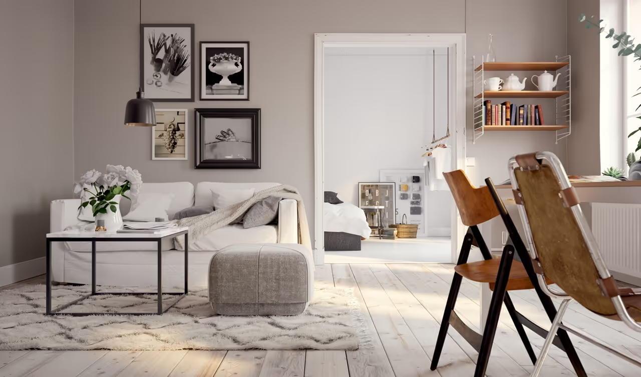 LUBA Immobilien UG - Immobilien - Gemütliches Wohnzimmer mit weißem Sofa, grauem Hocker, Marmor-Couchtisch mit weißen Blumen, gerahmten Bildern an der Wand, Holzboden und Blick in ein helles Schlafzimmer